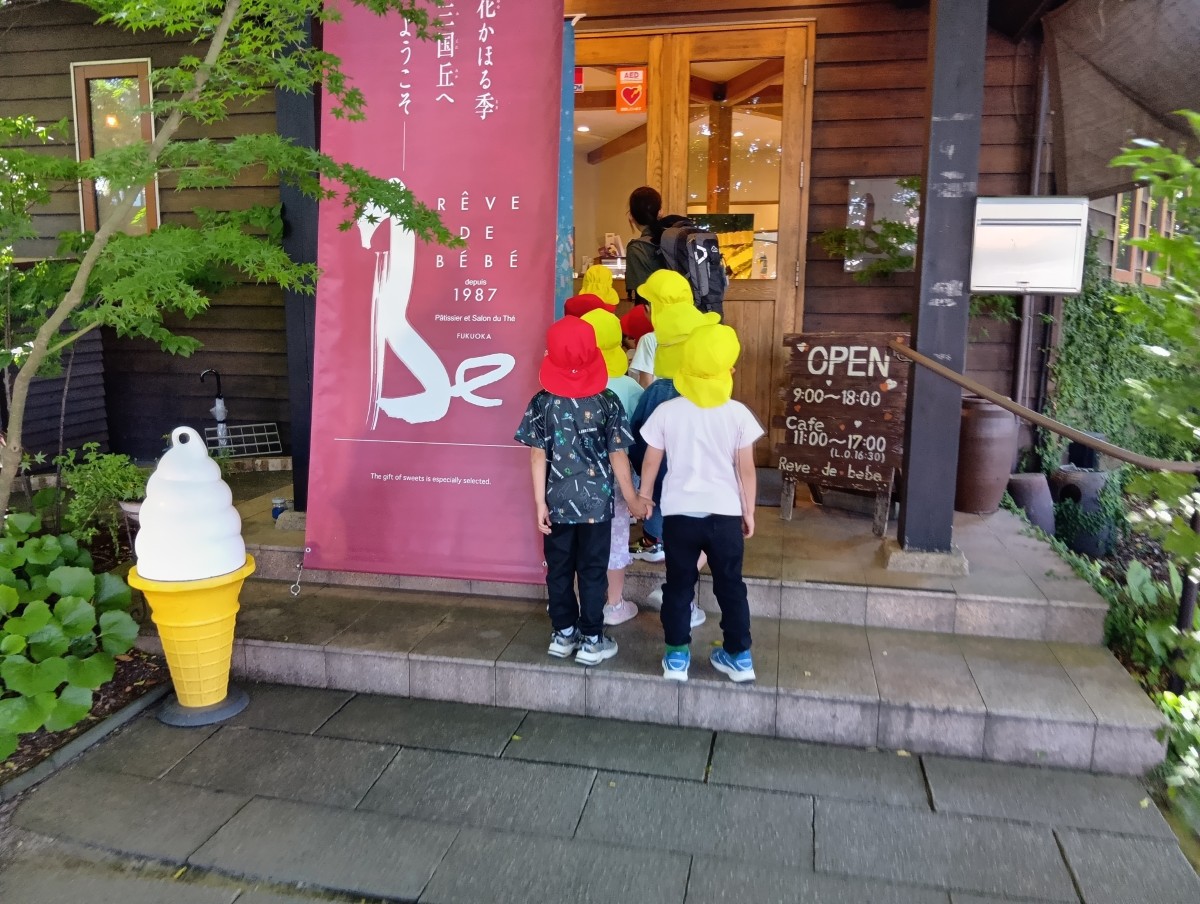 店の玄関先で友達同士手をつないで並ぶ子どもたちとスタッフの後ろ姿