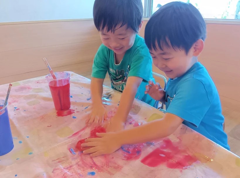 二人の子どもが、赤と青のスライムを机の上で触っている