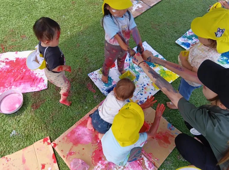 屋上庭園のボディペイントで描かれた段ボールや紙の上には、全身に絵の具を付けた子どもたちと大人がいる