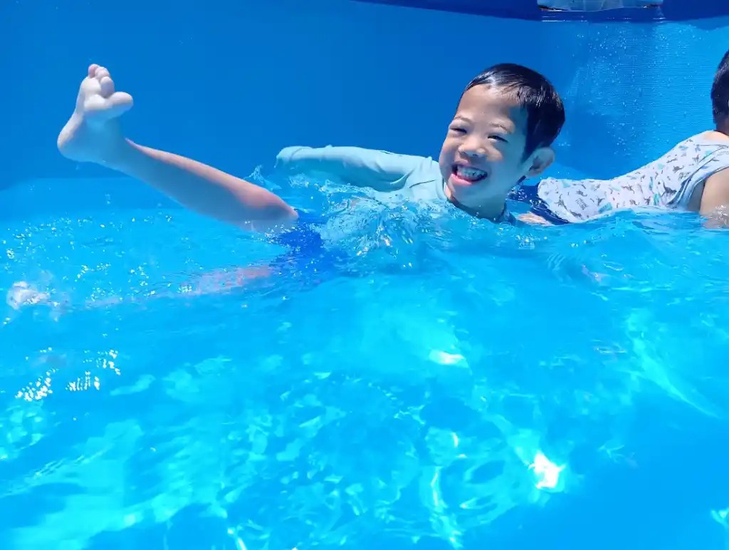 プールの中で、一人の子どもが楽しそうな表情で横向きになって足を上げている