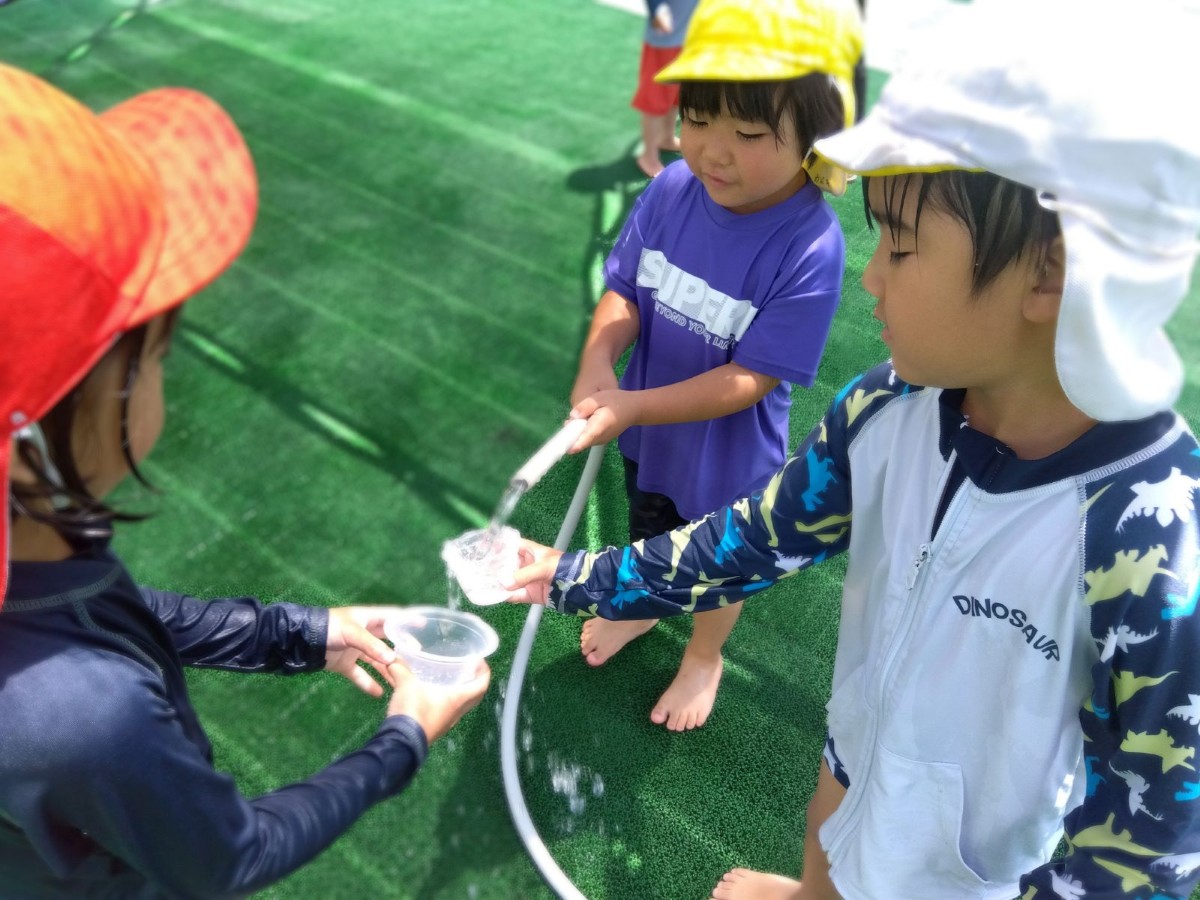 一人の子どもが水が出ているホースを持ち、他の子どもたちはホースの水を持っているカップに注いでいる
