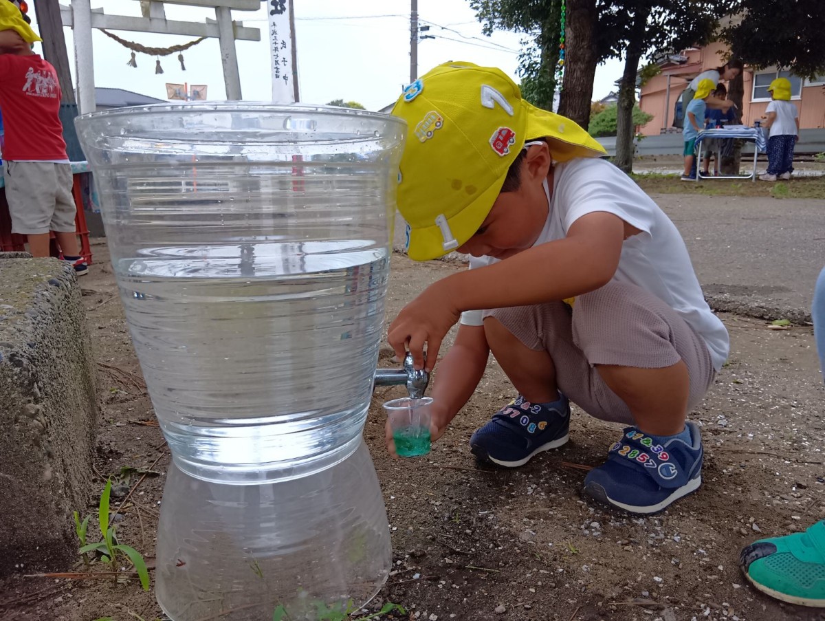 一人の子どもは色水の入ったカップを持って水道場へ行き、水を足している