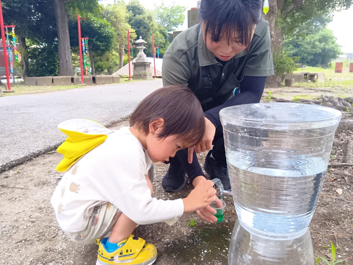 水道場では、大人が蛇口の水を出し、子どもは色水が入ったカップに水が足されていく様子を見ている