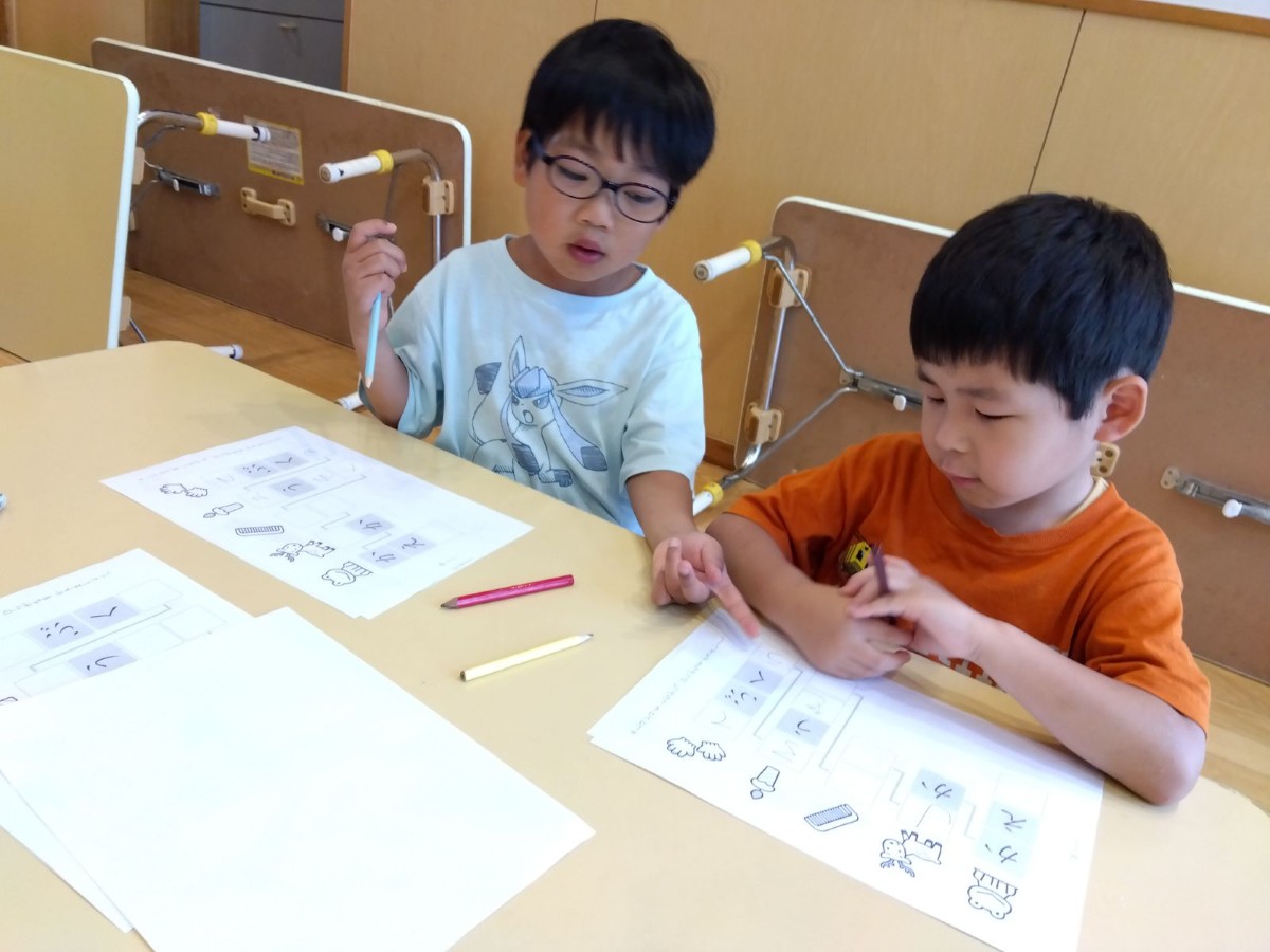 子どもたちは穴埋めワークをしており、一人の子どもが隣の友達のワークを指さして話しかけている