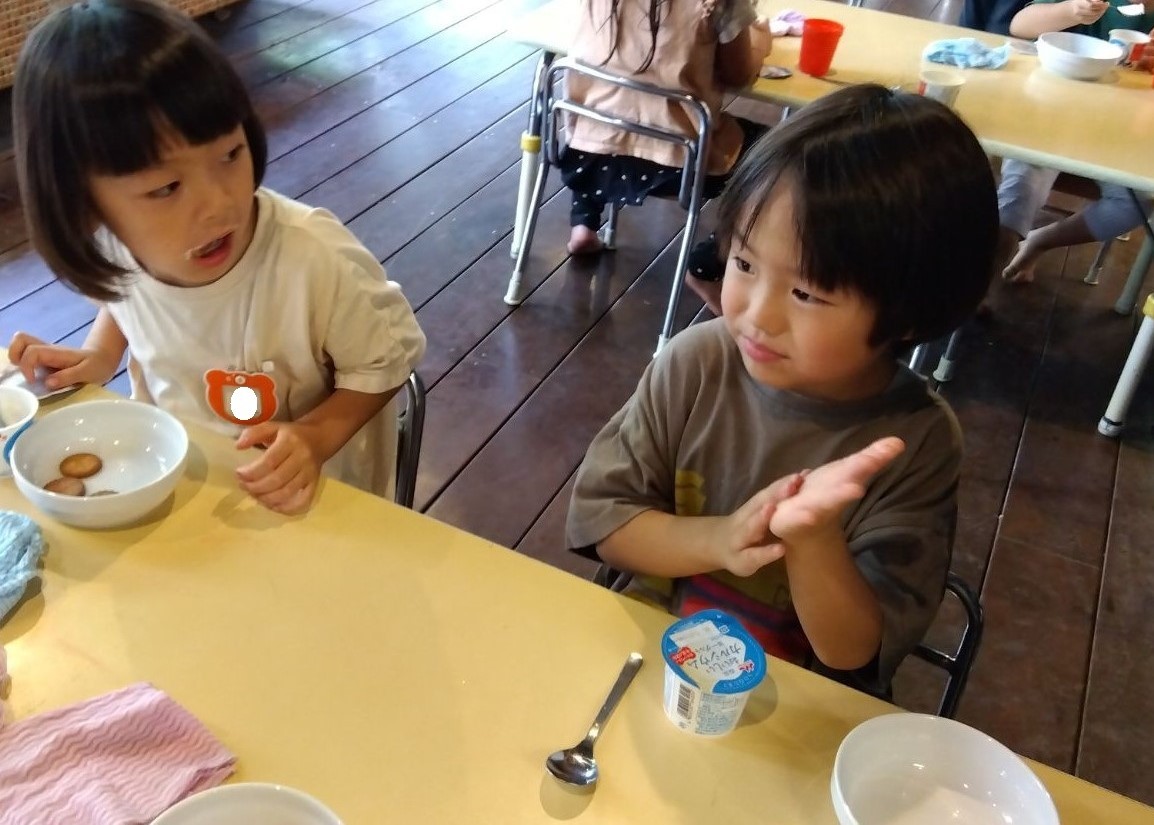 机の上に蓋の閉まっているヨーグルトが置かれており、目の前に座る子どもが困った表情をしている