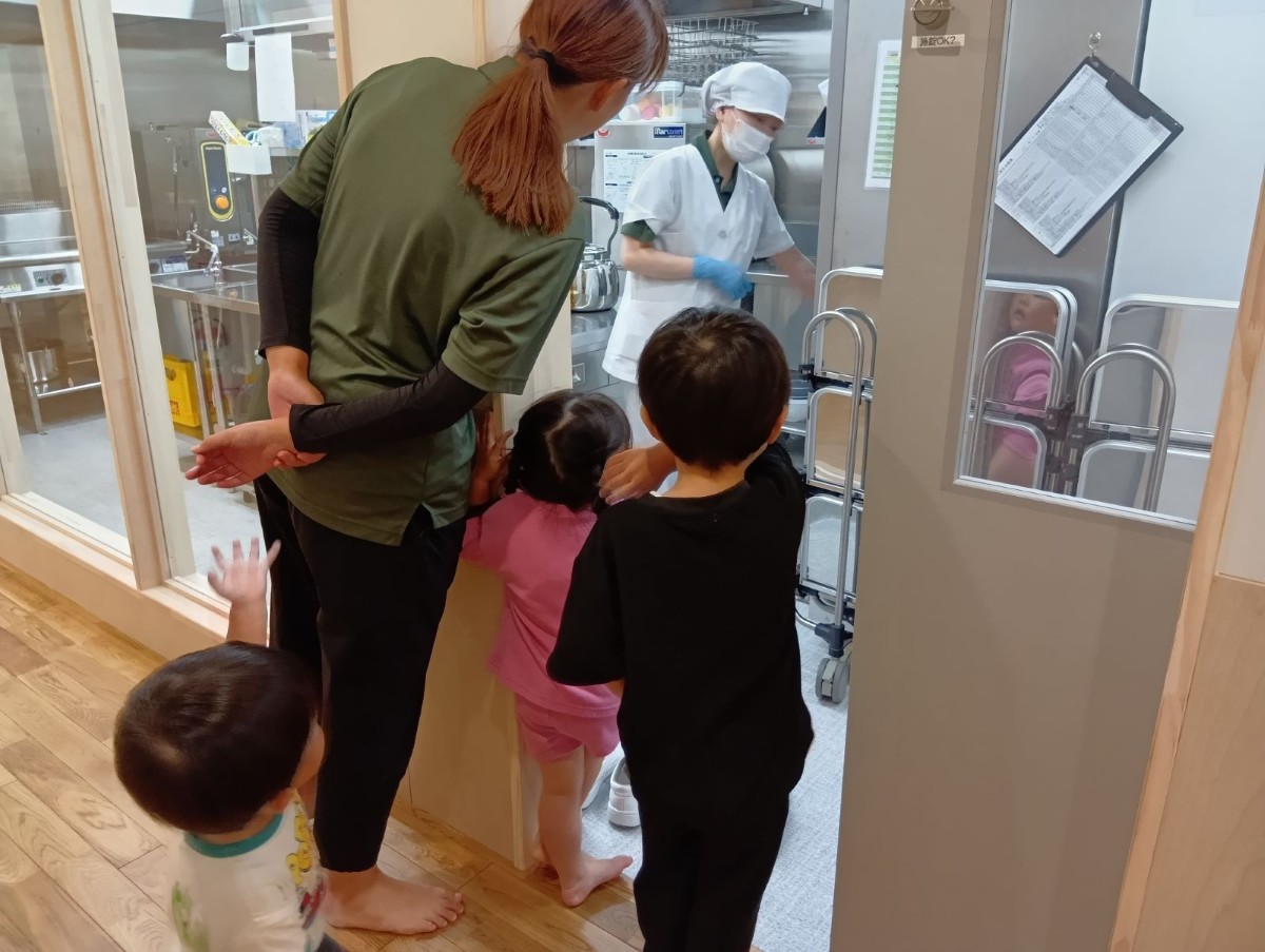スタッフと子どもたちが調理室の扉を開けて中にいるスタッフを見ている