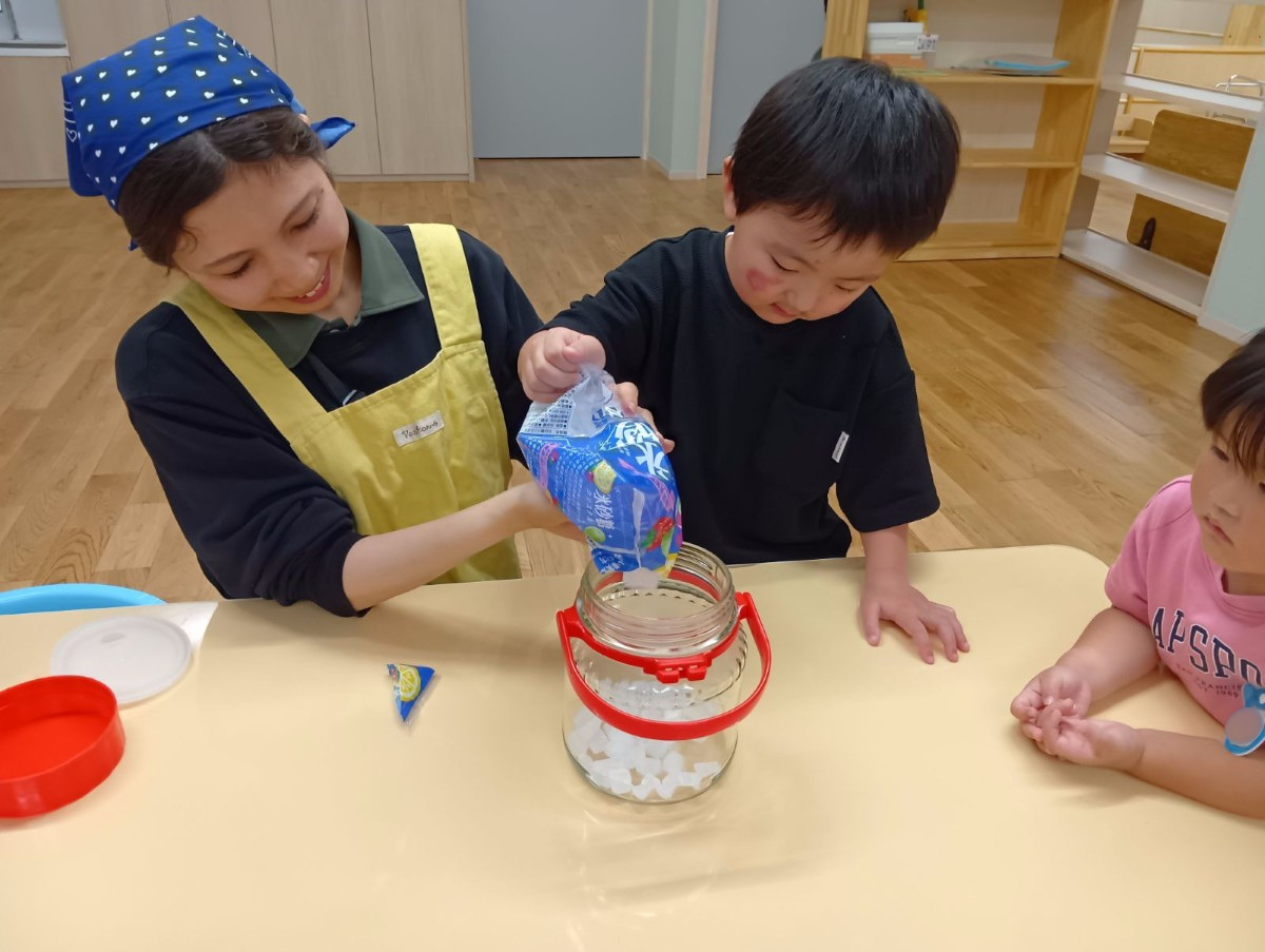大人と子どもが一緒に角砂糖の袋を持ち、袋を傾けて瓶の中に砂糖を入れている