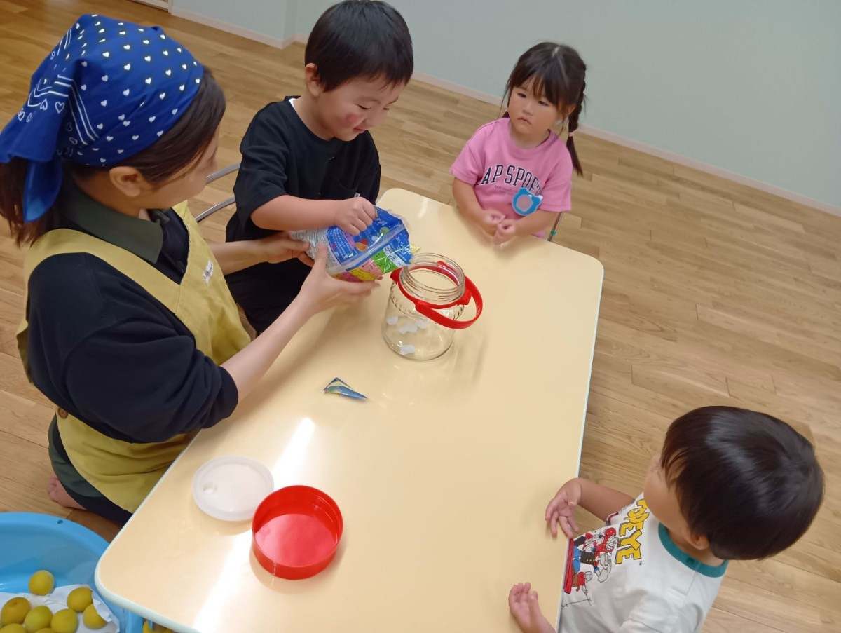 一人の子どもが砂糖を瓶の中に入れており、2人の子どもが順番を待っている
