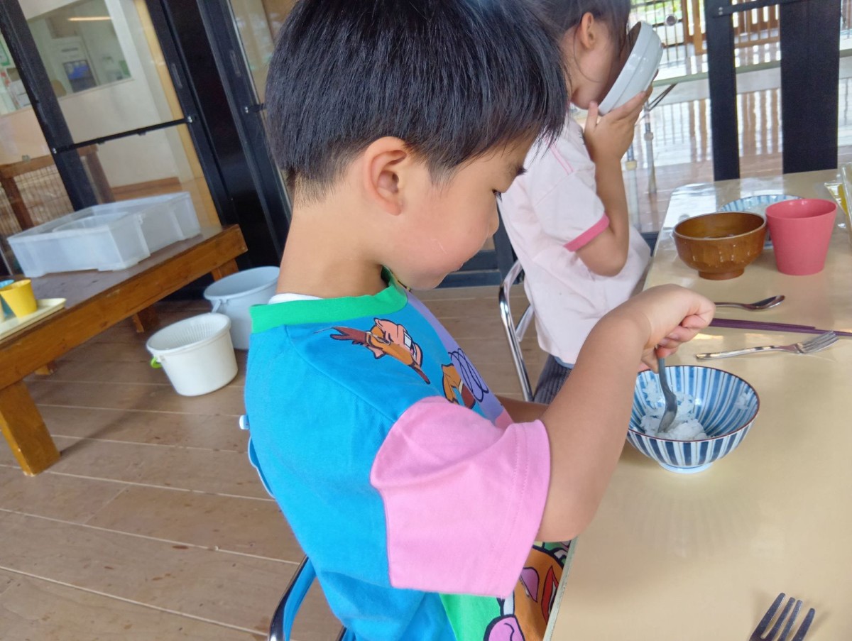 縁側に机が置かれ、子どもが食具を使って給食を食べている