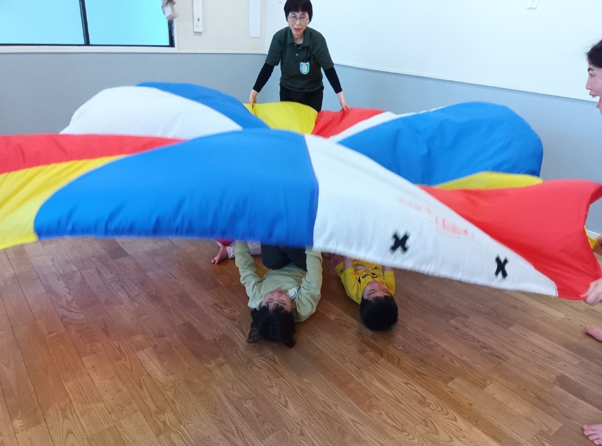 パラバルーンを大人が持ち、子どもたちはパラバルーンの下で横たわっている