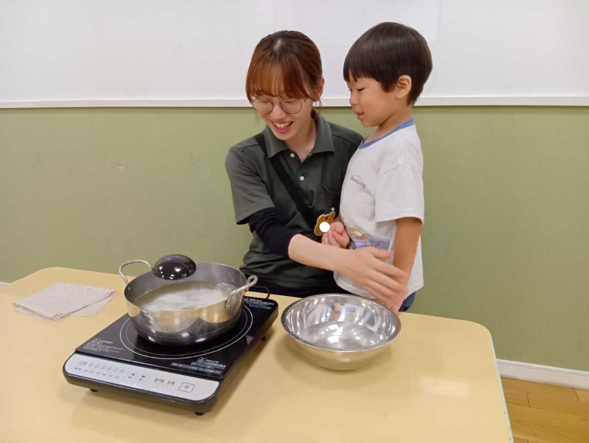 一人の大人と一人の子どもは、梅シロップをIHコンロで加熱して灰汁が出ている様子を見ている