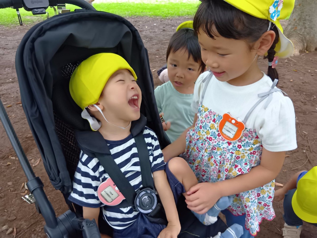 乳母車に乗っている子どもと隣に立つ子どもが目を合わせて笑い合っている
