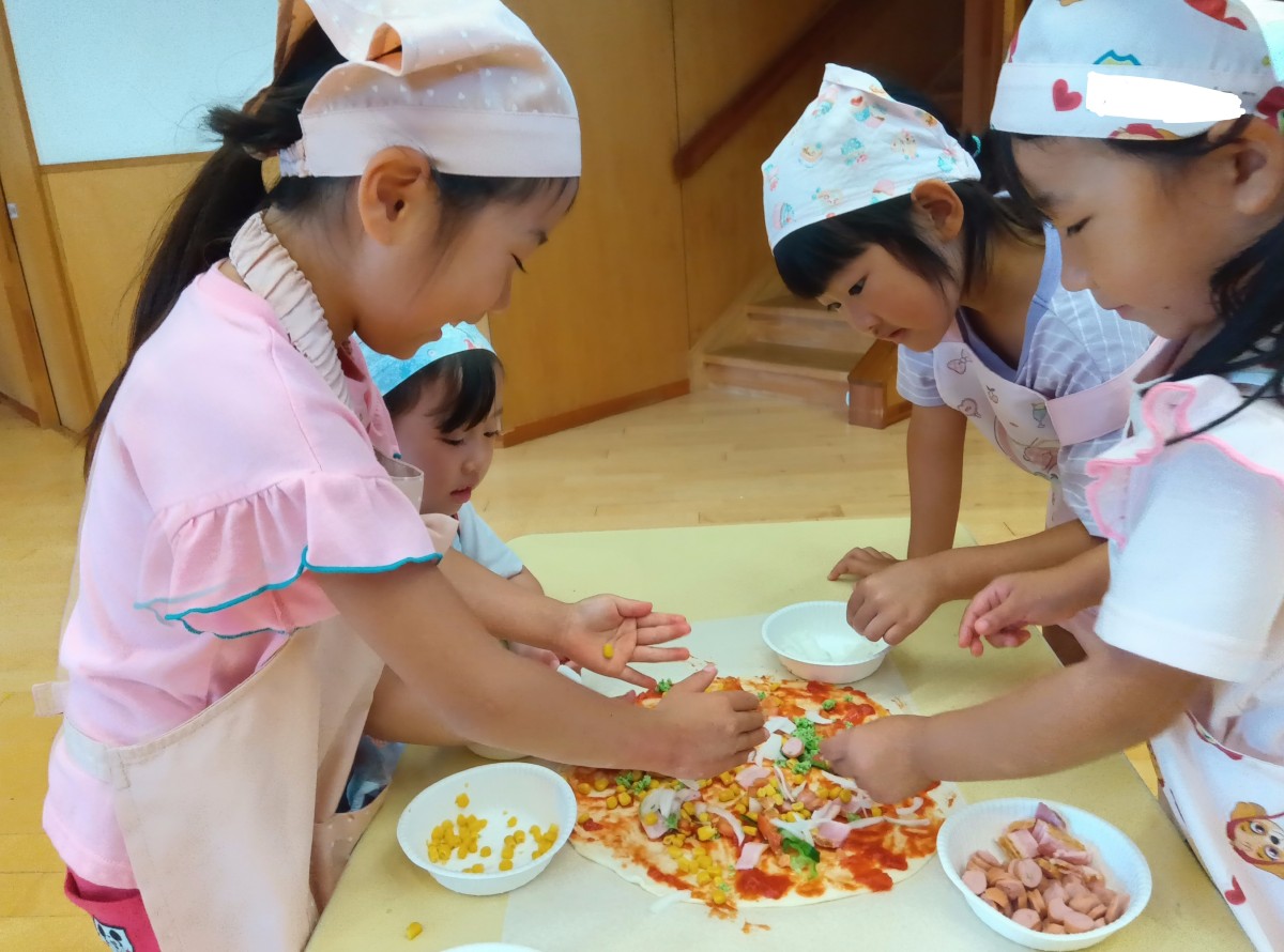 大きく伸ばした一つのピザ生地の上に、子どもたちは玉ねぎやコーン、ソーセージなどをトッピングしている