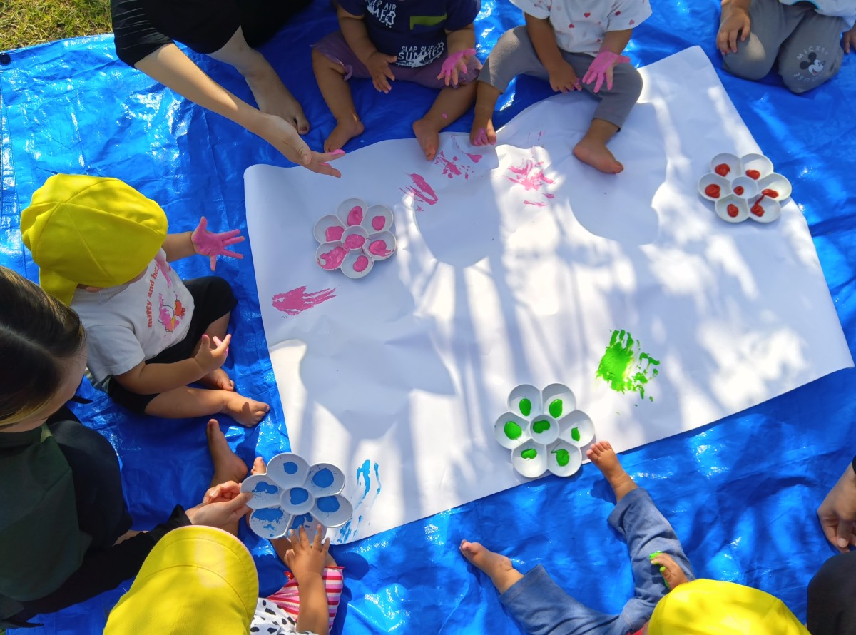 子どもの掌に絵の具を付けると、子どもは掌を広げたり自ら絵の具を指先で取ったりしている