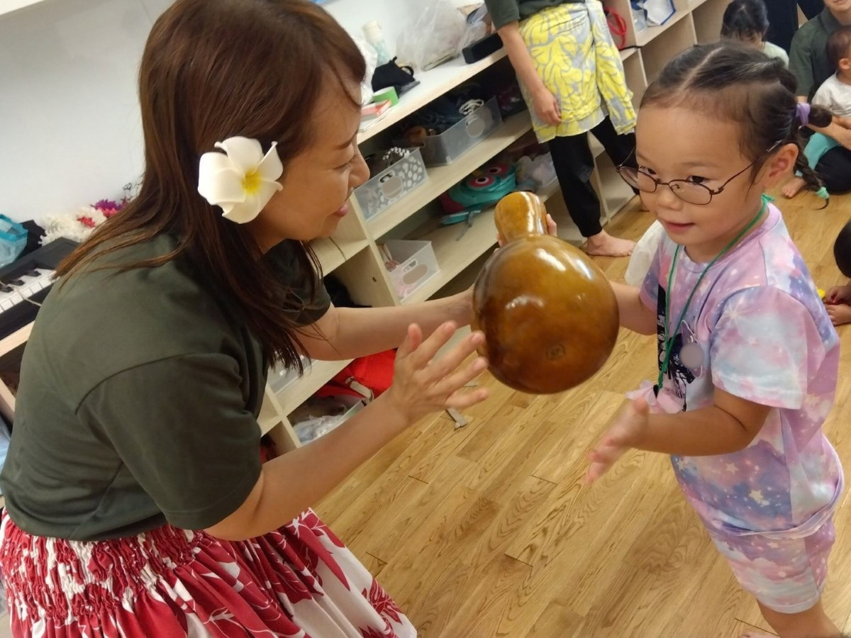 大人が手に持っている楽器を子どもも一緒に片手に持ち、反対の手では楽器を叩こうとしている