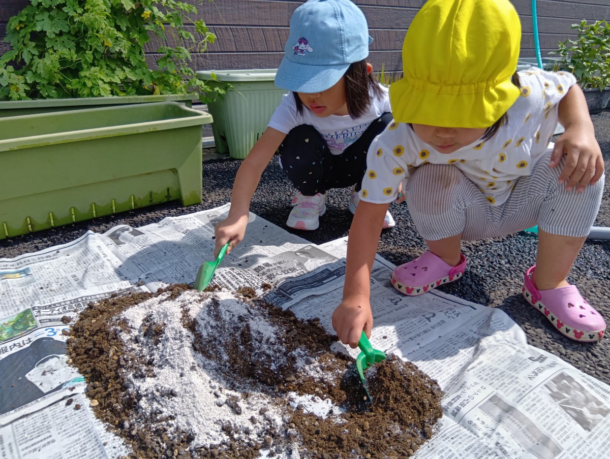 新聞紙の上には土と肥料を広げてあり、先の二人の子どもがスコップを使って混ぜている
