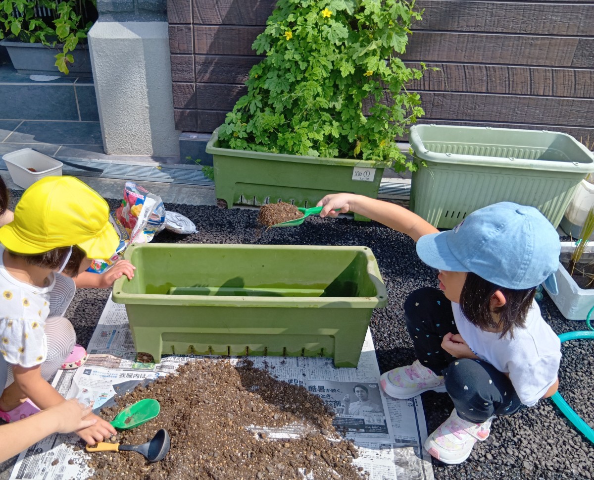 二人の子どもが、スコップを使ってプランターに肥料を混ぜた土を入れている