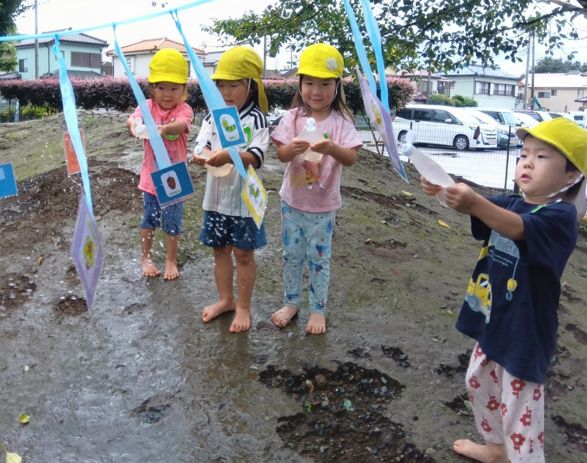 園庭で、子どもたちが水の入ったマヨネーズ容器を持って的をめがけて水を飛ばしている