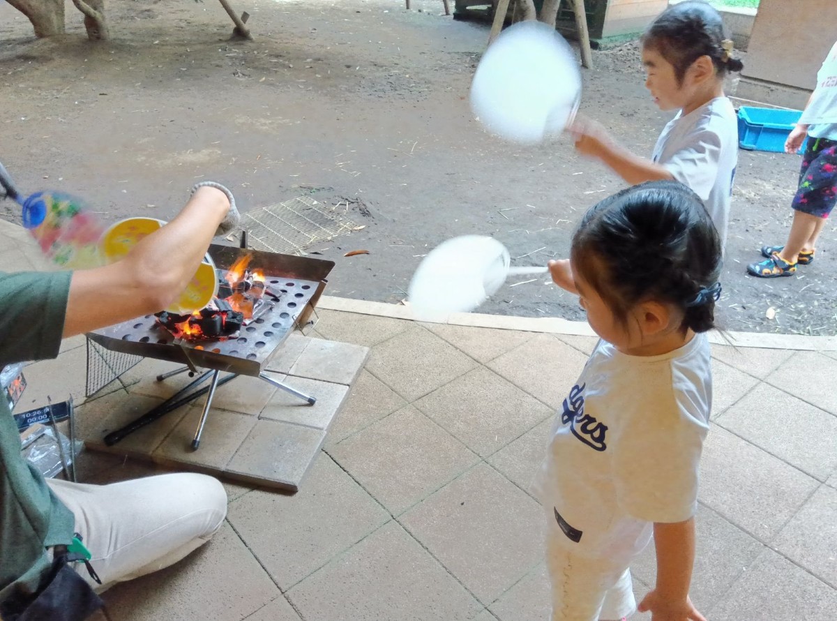 園庭では、団扇で二人のこどもと大人で火を扇いでいる