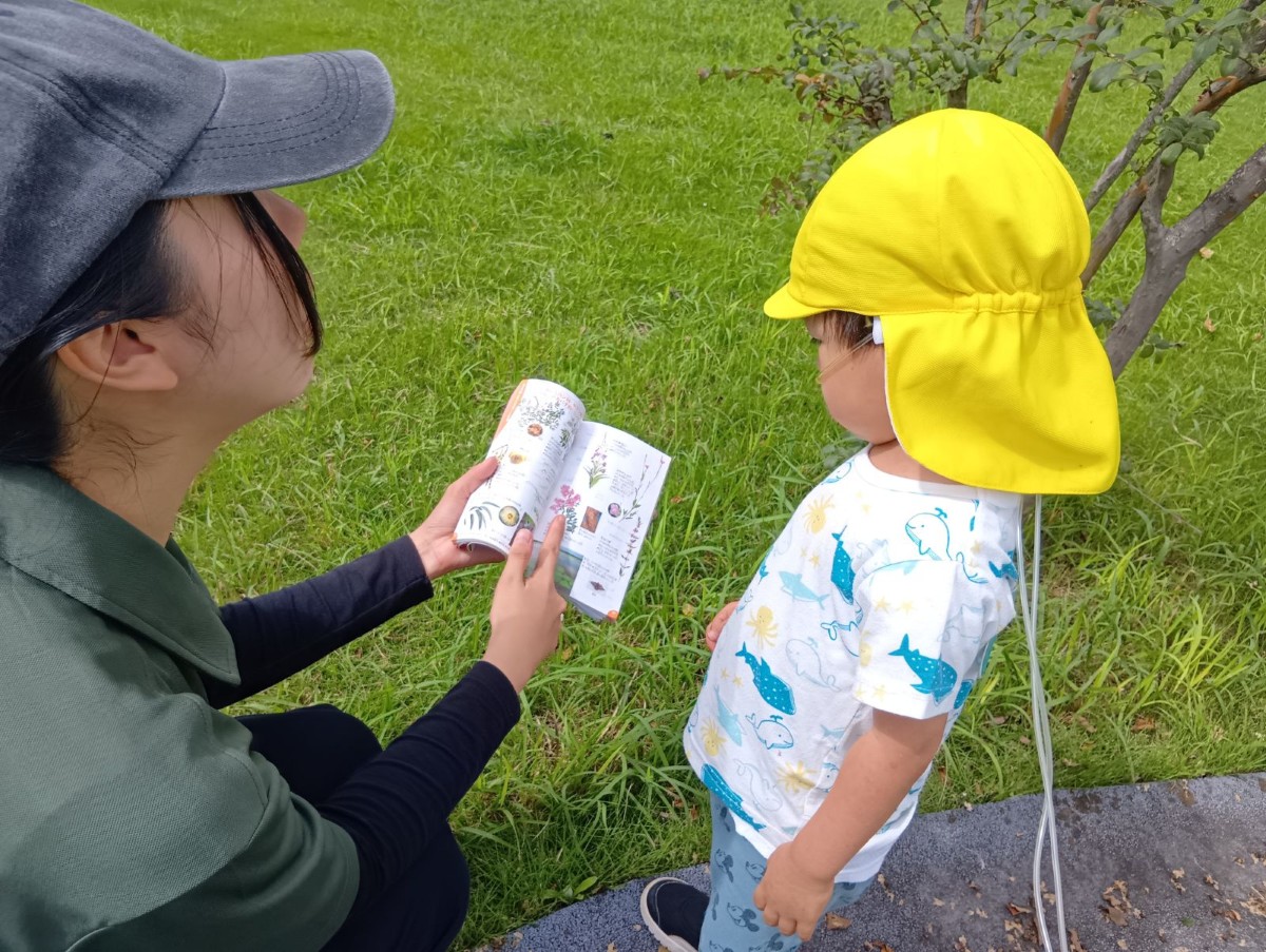 スタッフが花の図鑑を開いて持ち、隣にいる子どもはその図鑑を見ている