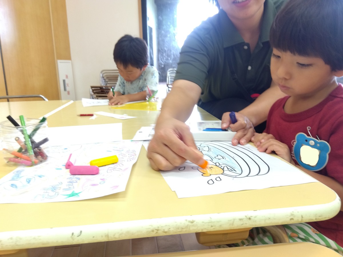 スタッフが塗り絵を塗り、一人の子どもがその様子を見つめている