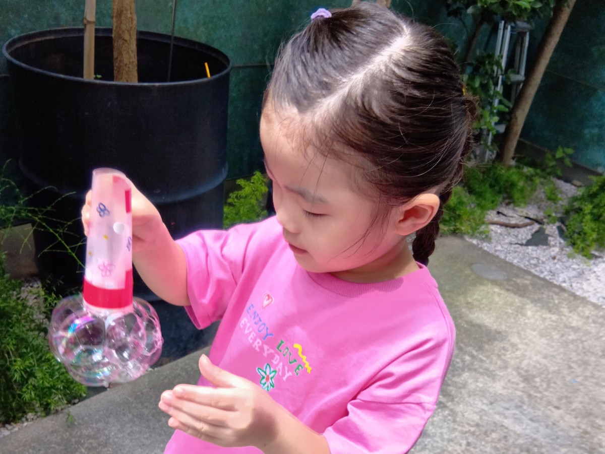 一人の子どもがシャボン液のついたシャボン玉の道具を片手に持ち、下から出てくるシャボン玉の泡を見つめている