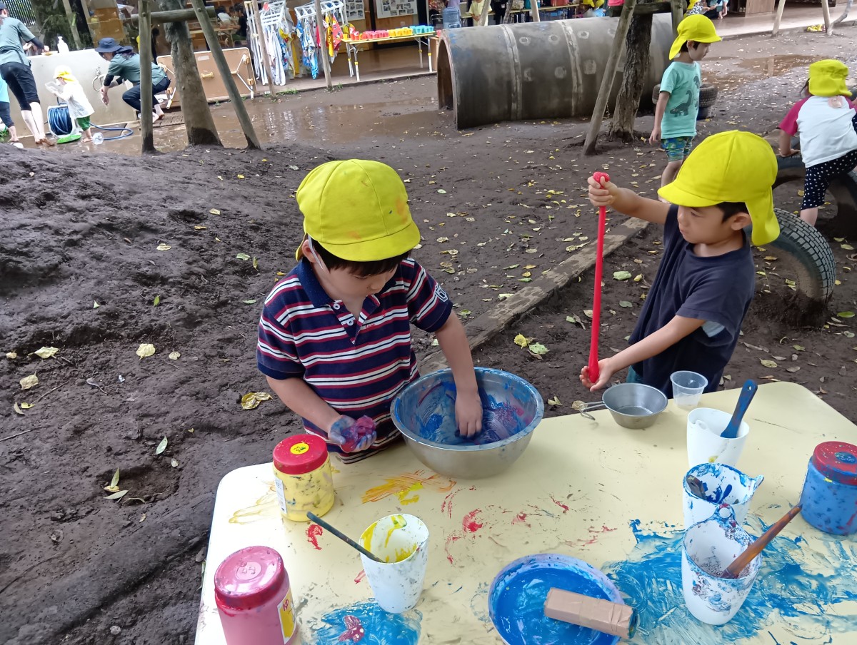 園庭では、二人のこどもがスライムを手で触って遊んでいる