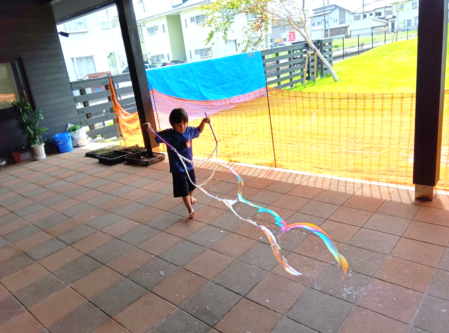 一人の子どもが、毛糸が付いた棒を手に持ち、長いシャボン玉を作り出している