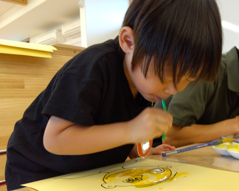 一人の子どもがストローを口にくわえて、吹き絵で絵の具を吹いて画用紙に色を付けている