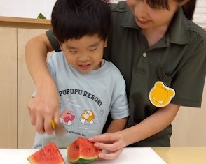 スタッフが子どもの手に添えながら、スイカを包丁で切っている