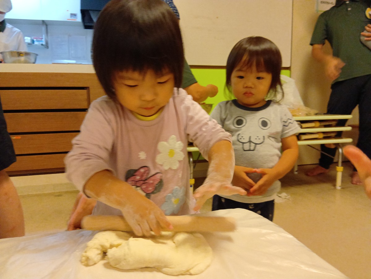 一人の子どもが麺棒を使ってうどんの生地を伸ばそうとしている